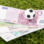 selective focus of toy soccer ball and euro banknotes on green grass, sports betting concept